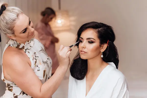 Carly applying eyeshadow to a dark-haired bride