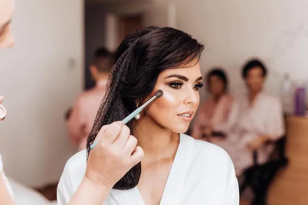 Makeup brush sweeping across a dark-haired bride's cheek