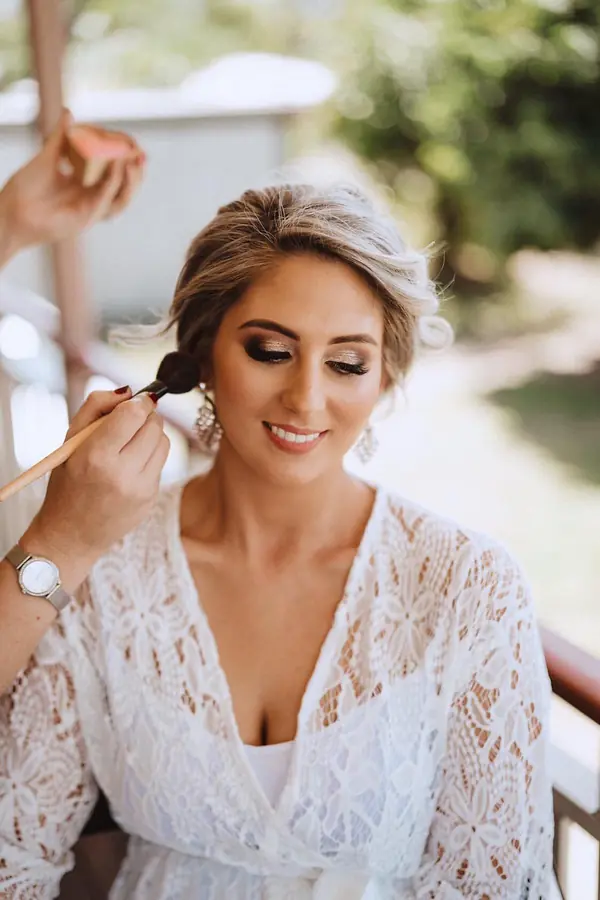 Blonde bride in a lace robe having her makeup applied
