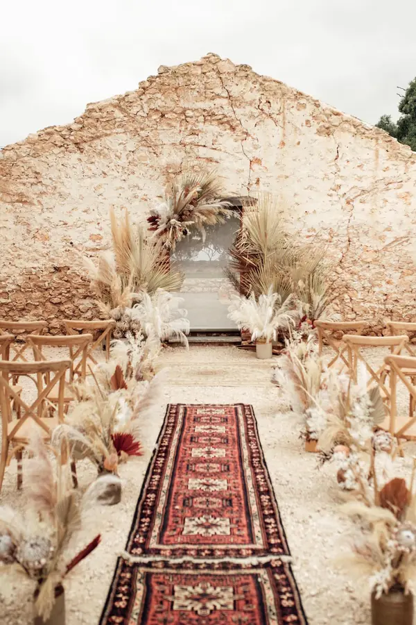 Boho ceremony aisle with a woven rug and pampas grass