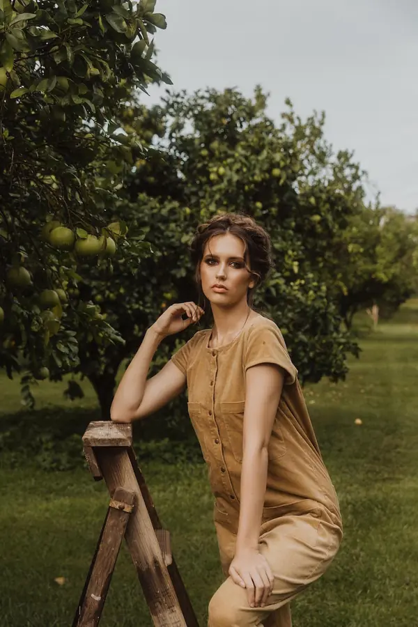 Model leaning on a wooden ladder in an orchard