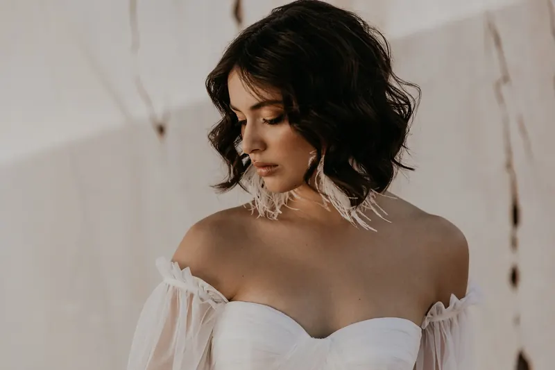 Bride with soft bronzed eyes and a nude lip, wearing feather earrings
